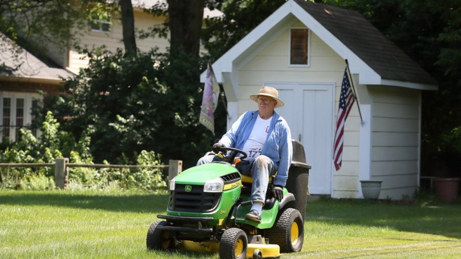 Homeowner mowing yard with shed in background